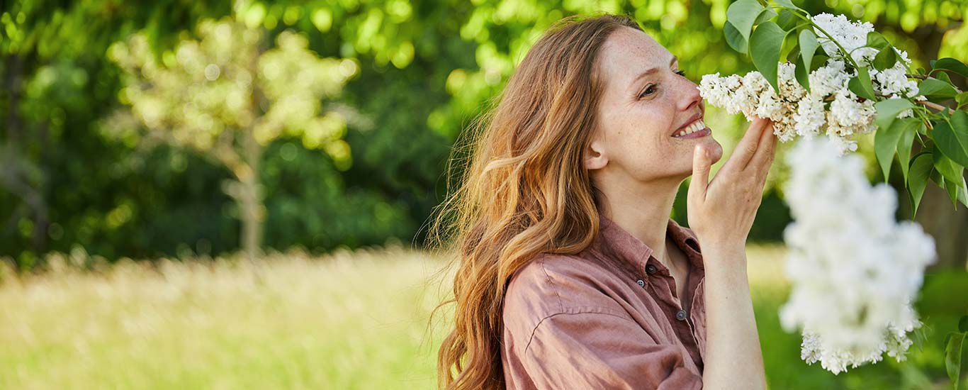 Vrouw ruikt aan een bloesem aan de boom.